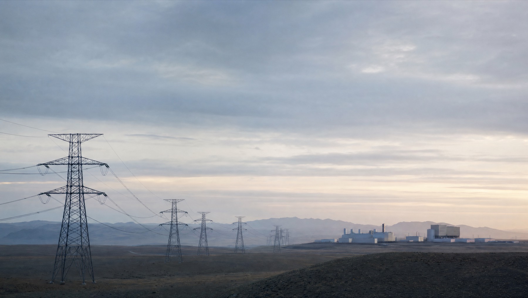A transmission corridor crossing open country toward a distant facility at first light.