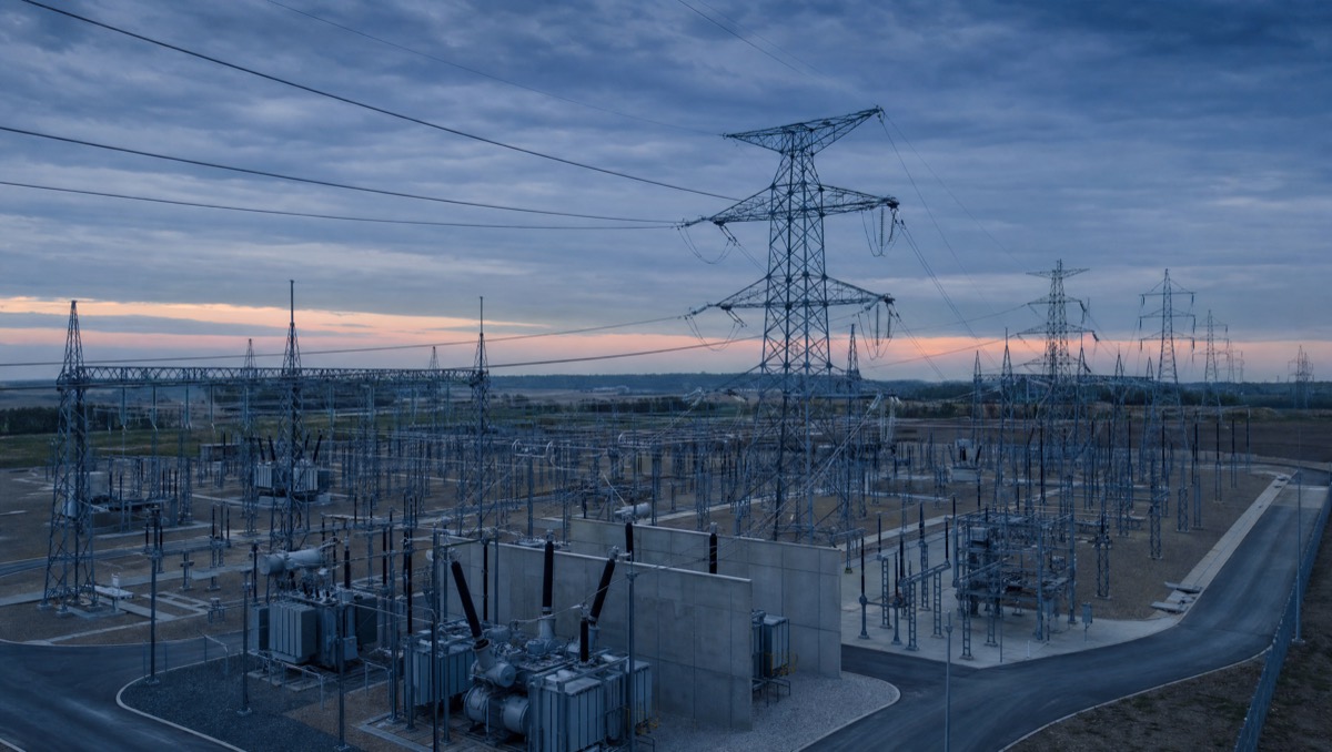 A high-voltage transmission substation and lattice towers at dusk.