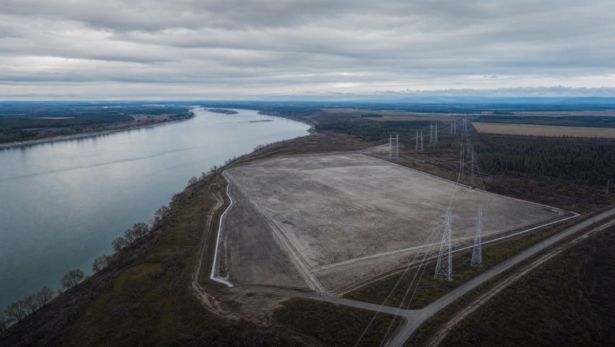 Aerial view of an undeveloped candidate site beside a river with a transmission corridor crossing one edge.